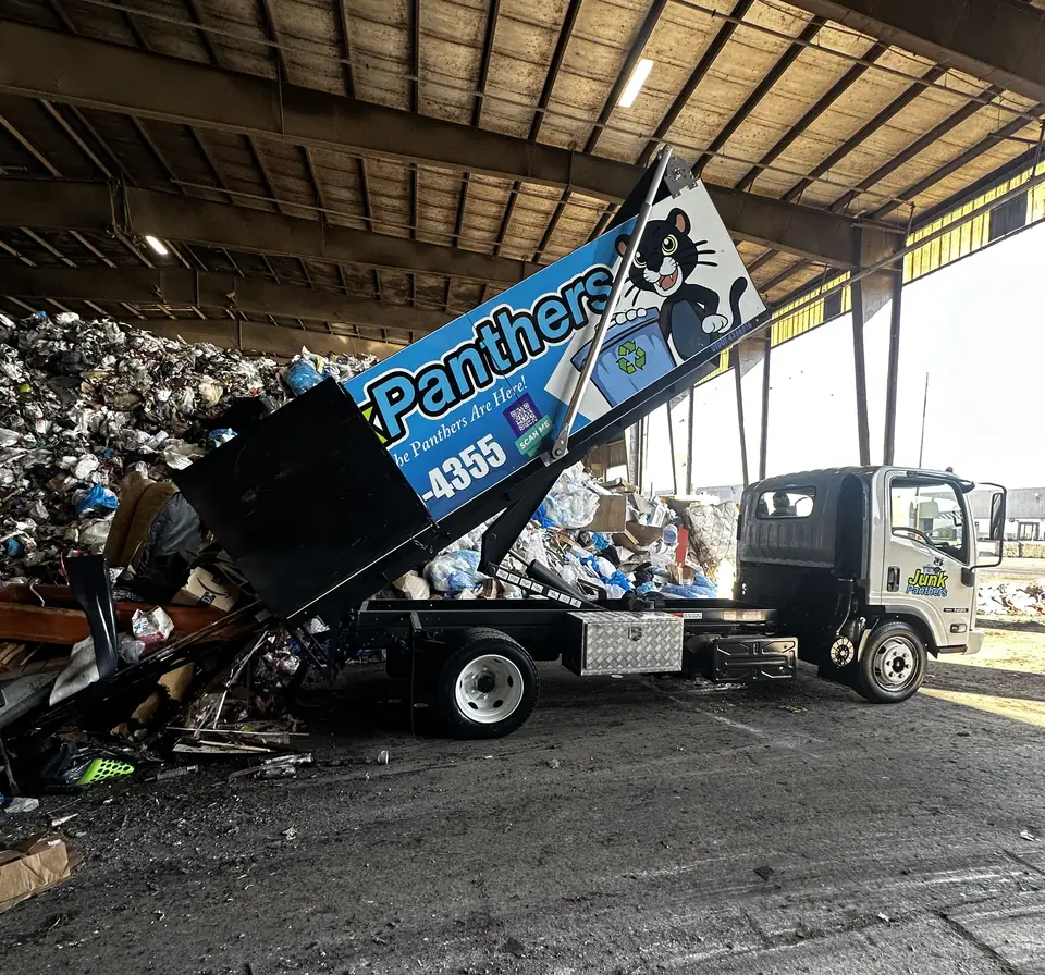 Junk Panthers truck with its dump body raised, unloading debris inside a transfer station