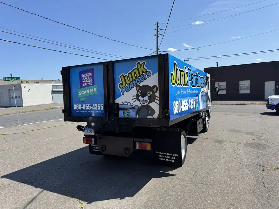 Rear view of a Junk Panthers dump truck with the panther mascot, phone number, and QR code on the wrap